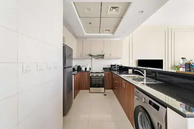 a kitchen with white cabinets and a stainless steel refrigerator at Silkhaus Modern Studio in Reef Residence at JVC in Dubai