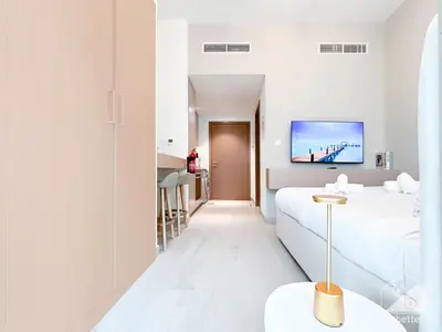 a white room with a bed and a tv on the wall at Cozy Studio with Balcony & Stunning Views in Dubai