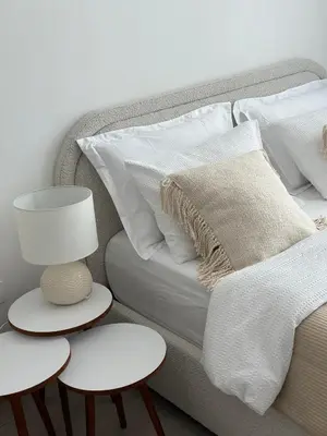 a bed with white pillows and a lamp and two tables at Cozy studio apartment in Jumeirah Village Circle in Dubai