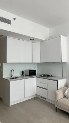 a kitchen with white cabinets and a sink and a couch at Cozy studio apartment in Jumeirah Village Circle in Dubai