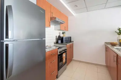 a kitchen with a stainless steel refrigerator and wooden cabinets at Frank Porter - Al Arta 4 in Dubai