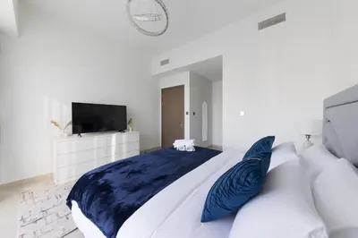 a white bedroom with a large bed with blue pillows at Spacious 3BR plus maids Burj Khalifa View in Dubai