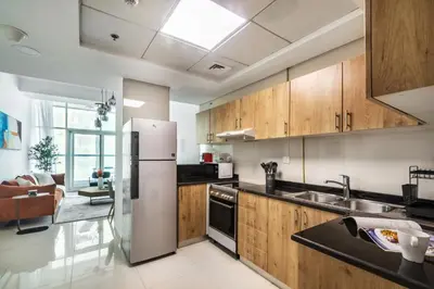 a kitchen with wooden cabinets and a stainless steel refrigerator at ShoresInn - Waterfront in Heart of Dubai Marina in Dubai