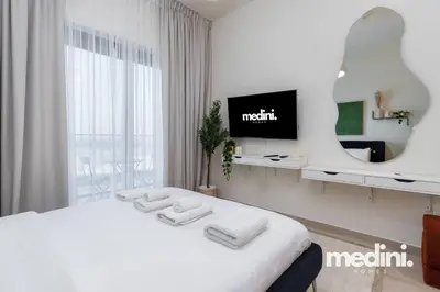 a white bedroom with a bed and a tv at Cozy Studio in Azizi Riviera - Dubai in Dubai
