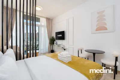 a white bedroom with a bed and a table and a tv at Studio in Bloom Height - JVC - Dubai in Dubai