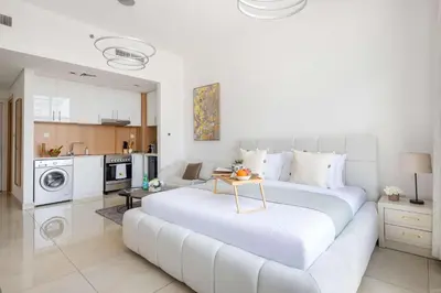 a white bedroom with a large bed and a kitchen at Frank Porter - Square Tower in Dubai