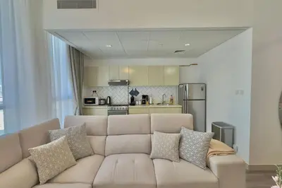a living room with a couch in front of a kitchen at Elegant 1BR Midtown Near City Center Meaisem by Vibel in Dubai