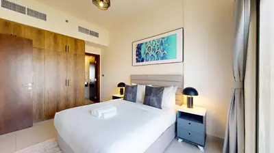 a bedroom with a white bed and a wooden cabinet at Locations I Binghatti Gate I Premium Modern 2BR I Skyline & Community Views I Spacious & Comfortable Stay in Dubai