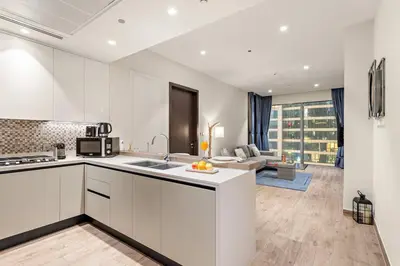 a kitchen with white cabinets and a living room at Dubai Marina 1BR with Pool Near Shops & Restaurants in Dubai