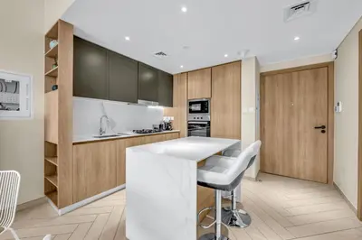 a kitchen with a white counter and wooden cabinets at Waves - Comfortable JVC Apt with Balcony and Maids Room in Dubai