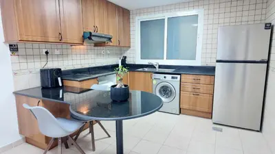 a kitchen with a table and a white refrigerator at Luxury OneBedroom Apartment next to Barasti Beach in Dubai