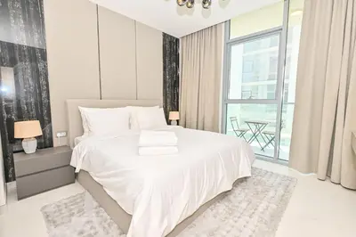 a white bedroom with a white bed and a window at Stunning 1BR Retreat with Crystal Lagoon Views! in Dubai