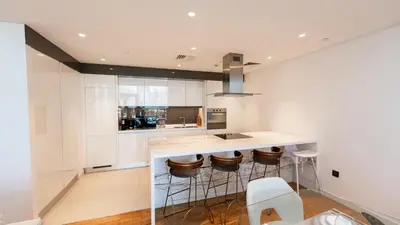 a kitchen with white cabinets and a counter with stools at Bluewaters Island - Luxury 2BR with Ain View by TLRE Holiday Homes in Dubai