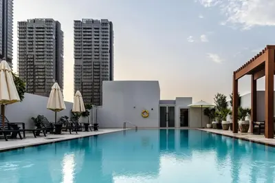 a swimming pool with chairs and umbrellas and buildings at Waves - Luxury Meets Comfort, Modern 1BR in JVCs Luma22 in Dubai