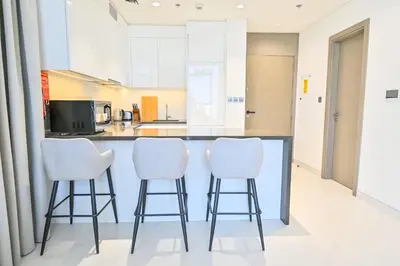 a kitchen with white stools at a counter at Family-friendly 1 Bedroom in District One Meydan in Dubai