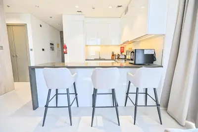 a kitchen with a counter with three white bar stools at Modern 1BR in District One Meydan in Dubai