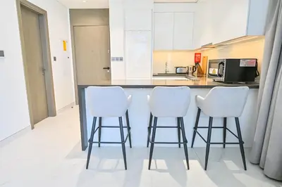 a kitchen with three white bar stools in front of a counter at Luxury and Spacious 1 Bedroom in District One Meydan in Dubai