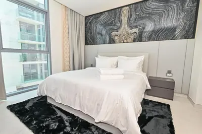 a bedroom with a white bed with a large window at 1BR by Dubai Crystal Lagoon in District One Meydan in Dubai