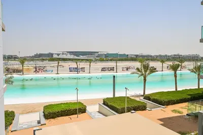 a large swimming pool with palm trees and a beach at 1BR Gem by Crystal Lagoon in District One Meydan in Dubai