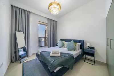 a bedroom with a bed with a window and a chandelier at Homes Beyond I 2 BR Apartment with Panoramic Creek View in Dubai