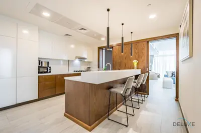 a kitchen with white cabinets and a bar with stools at Spectacular 4BR Penthouse with Assistant Room in Hameni Tower, JVC by Deluxe Holiday Homes in Dubai