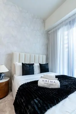 a bedroom with a large white bed with a black blanket at Nasma Luxury Stays - Cozy Urban Studio at Azizi Riviera 43 in Meydan in Dubai