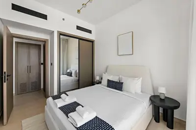 a white bedroom with a large bed and a table at Vayk - Modern 2BR Apartment in Dubai