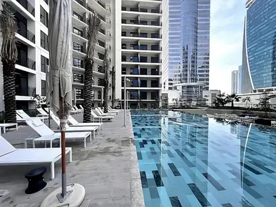 a swimming pool with white chairs and buildings at Citihome - 1BR with Huge Balcony & Easy Transport Access in Dubai