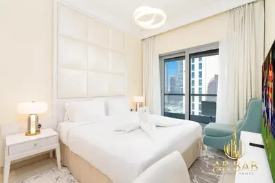 a white bedroom with a large bed and a chair at Damac Maison Mall Street - Royal 3BR - Burj Khalifa View - Near Dubai Mall in Dubai