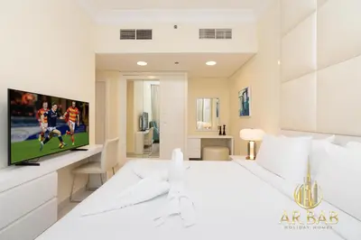 a white bedroom with a large white bed and a tv at Damac Maison Mall Street - Royal 3BR - Burj Khalifa View - Near Dubai Mall in Dubai