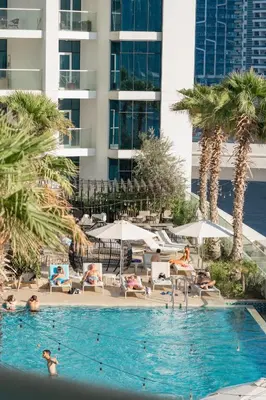a swimming pool with people sitting in chairs and umbrellas at DAMAC MAISON PRIVE - Lake View in Dubai
