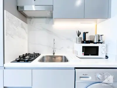 a white kitchen with a sink and a microwave at Breath taking Studio with Balcony & Stunning Views in Dubai