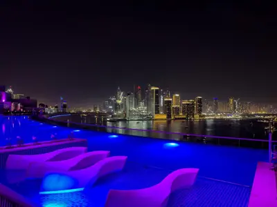 a pool with pink chairs and a city skyline at night at Beachfront 1 Bedroom Apartment on Palm Jumeirah with Stunning Sea Views and Rooftop Infinity Pool in Dubai