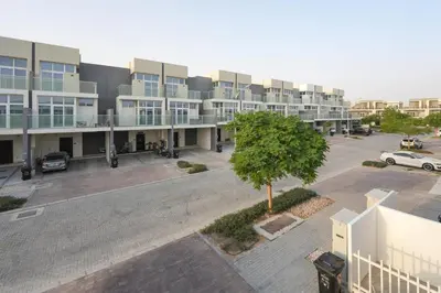 an apartment building with a parking lot and a tree at Luxurious 3BDR Serenity Awaits in Damac Hills 2 in Dubai