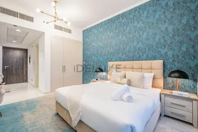 a bedroom with a large bed and a blue wall at Chic Studio in Damac Hills Carson B, Dubailand by Deluxe Holiday Homes in Dubai