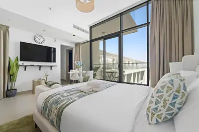a white bedroom with a large bed and a balcony at Modern Studio Near To Park in Dubai