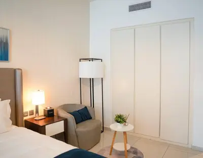 a bedroom with a bed and a chair and a lamp at Cozy Studio Business Bay in Dubai