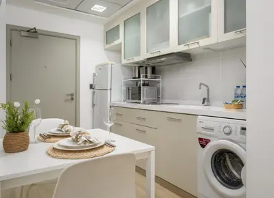 a white kitchen with a table and a washing machine at Modern studio near the beach in Dubai