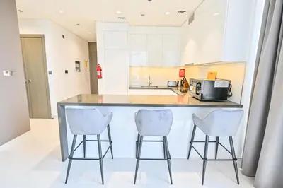 a kitchen with a counter and three bar stools at Stylish 1BR by the Lagoon in District One Meydan in Dubai