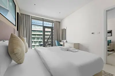 a white bedroom with a large white bed and a window at Chic Living 1 BHK with Beach Access in Dubai