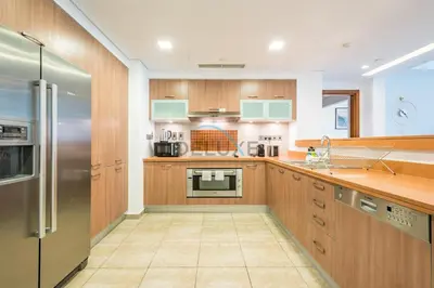 a kitchen with wooden cabinets and a stainless steel refrigerator at Chic 2BR Apartment with Pool View in Marina Apartment 6, Palm Jumeirah by Deluxe Holiday Homes in Dubai