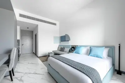 a white and blue bedroom with a bed and a desk at Modern Meydan Studio Apartment - 15 min Drive to Downtown Dubai Mall in Dubai
