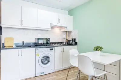 a white kitchen with a washing machine and a table at Luxe Studio with Upgraded Interior in Sports City in Dubai