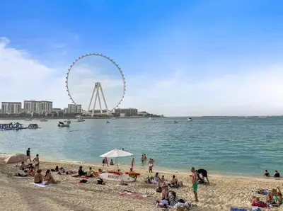 people on a beach with a ferris wheel in the background at 4BR Jumeirah Beach Stay with Dubai Eye Views & Near Marina Walk in Dubai