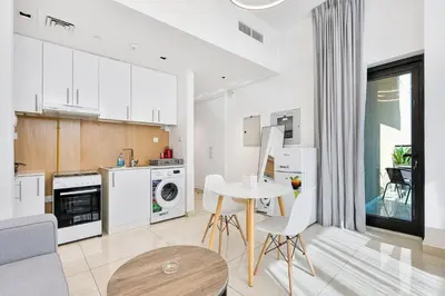 a kitchen with white cabinets and a table and chairs at Lovely Studio with Pool and Gym in Dubai