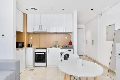 a kitchen with white cabinets and a white table at Lovely Studio with Pool and Gym in Dubai