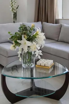 a glass coffee table with a vase of flowers on it at Frank Porter - Damac Cour Jardin in Dubai