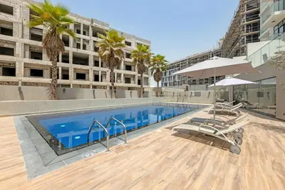 a swimming pool with chairs and umbrellas next to a building at Comfy JVC Studio Pantheon Comfort & Style by Vibel in Dubai