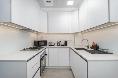 a white kitchen with white cabinets and a sink at New Charming Studio in JVC in Dubai