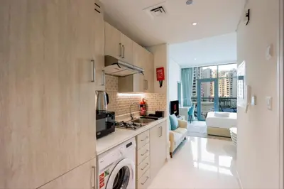 a kitchen with a washer and dryer and a living room at Exquisite Studio near Nakheel Mall by Livbnb in Dubai